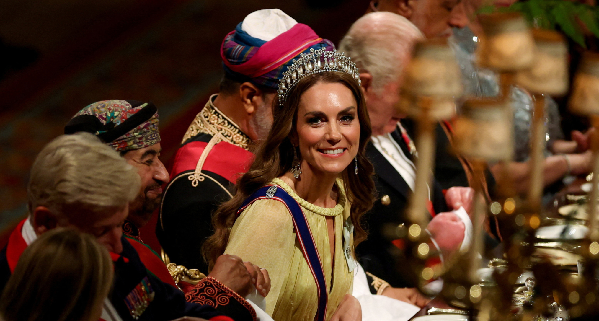 Princess Kate leaning forward in a yellow gown and tiara at a banquet table