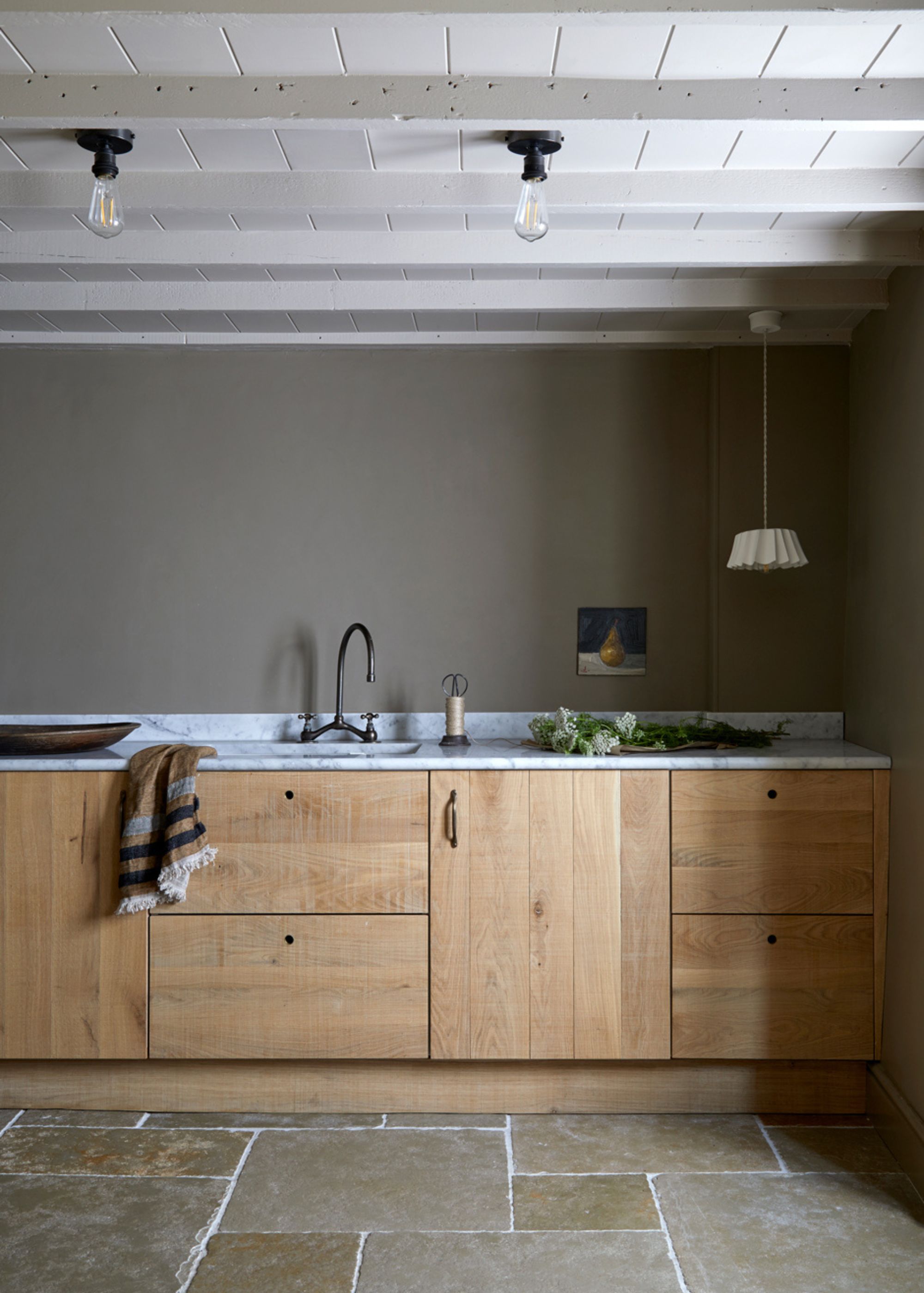 A boot room with dark gray-brown walls, wooden cabinets, flagstone flooring, and white marble countertops.