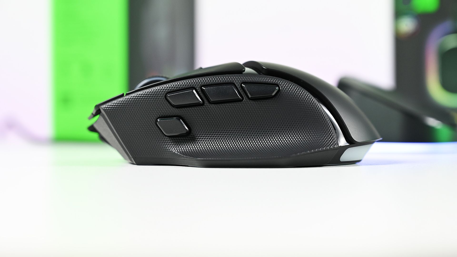 Left side profile of the black Razer Basilisk V4 Pro gaming mouse resting on a white desk, highlighting textured rubber thumb grips and multi-button controls.