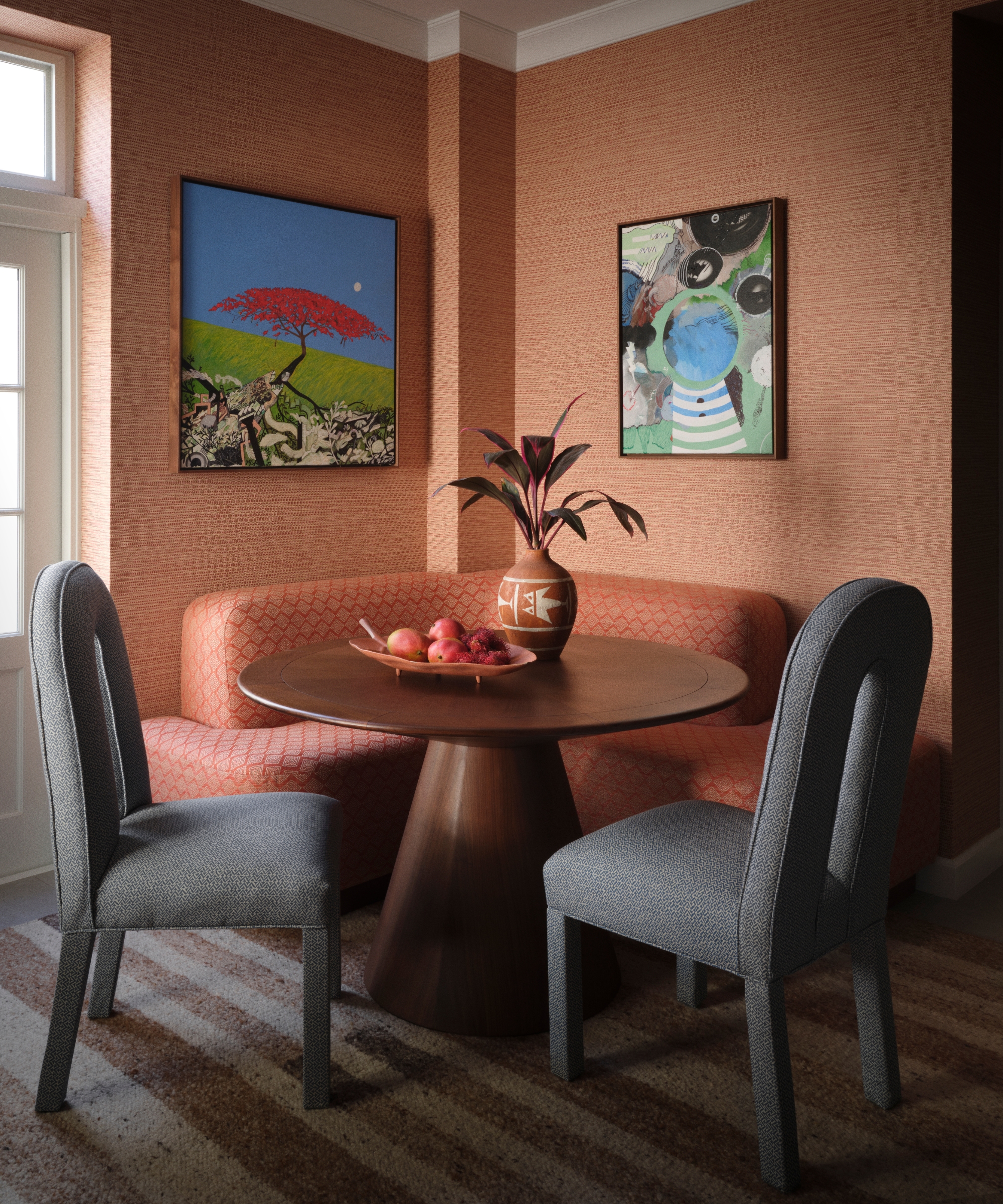Breakfast nook with coral banquette, round wood table, blue upholstered chairs, textured terracotta walls and colorful art.