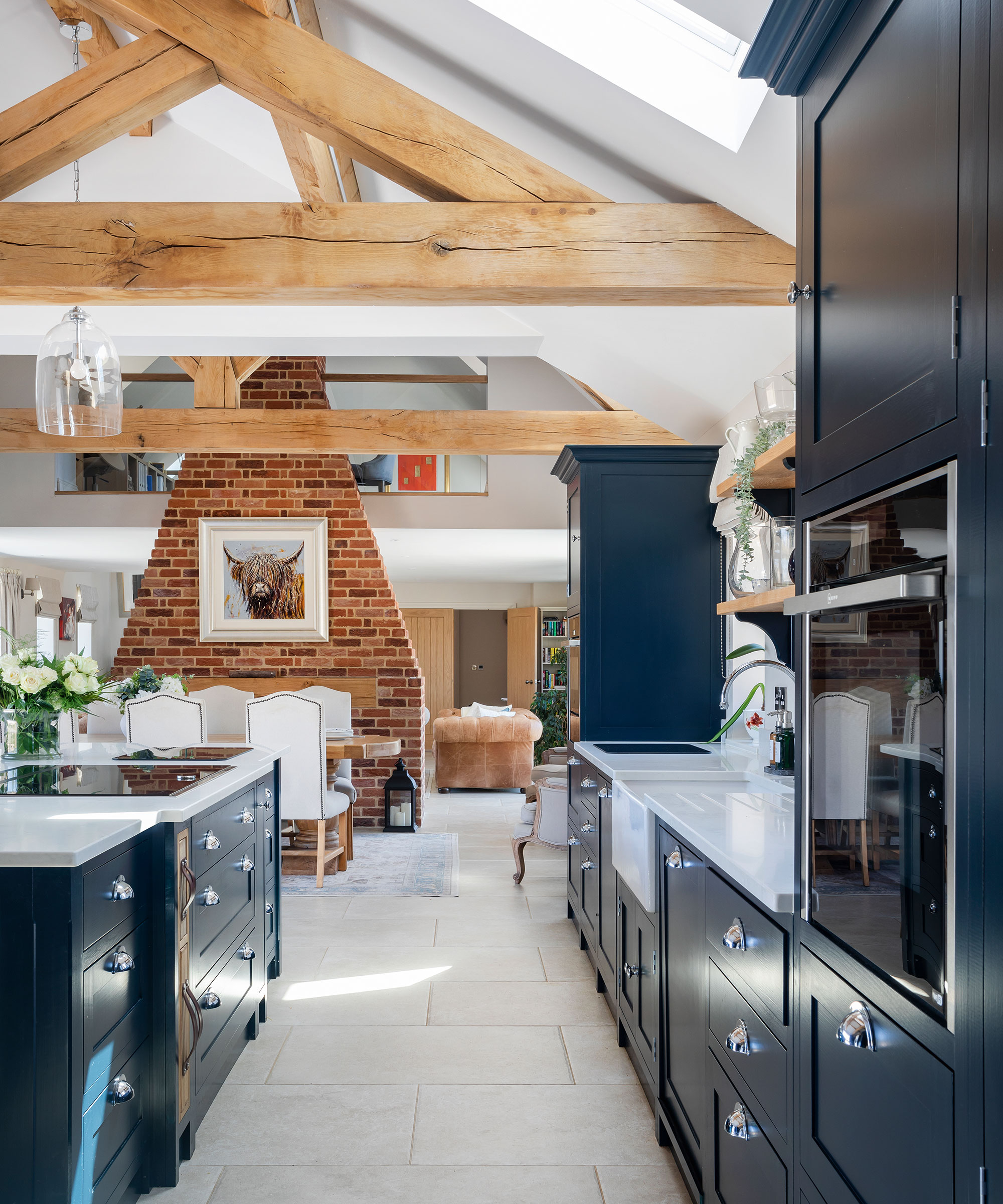 large open-plan kitchen-diner in a barn-style home with exposed oak beams and a central brick fireplace and chimney