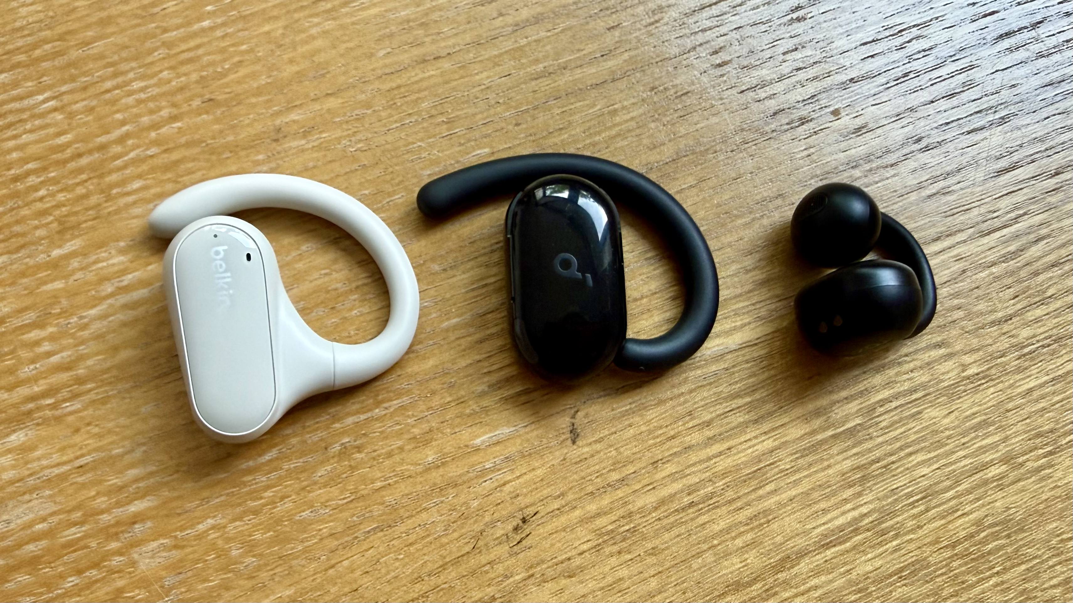One bud from three pairs of open earbuds all pair of an open earbuds test pictured on a wooden surface