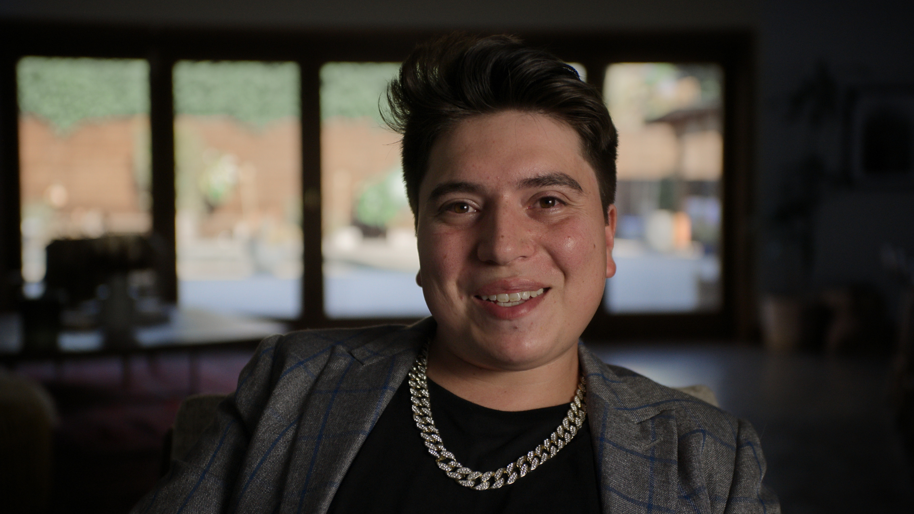 a man in a blazer black shirt and chain necklace in a still from the documentary spy high
