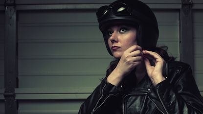 A woman buckles the chin strap to her motorcycle helmet.