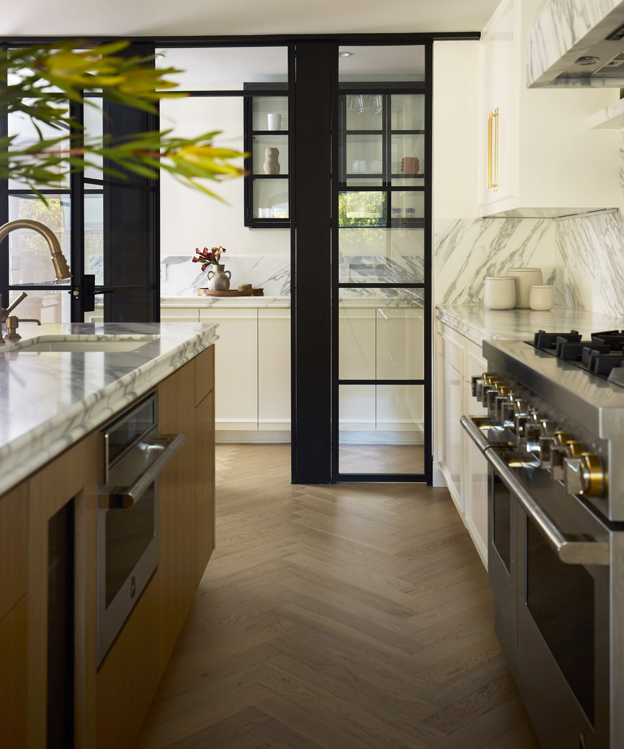 looking down a kitchen with cabinets on one side and a stainless steel oven on the other, with crittal doors at the end leading to a pantry