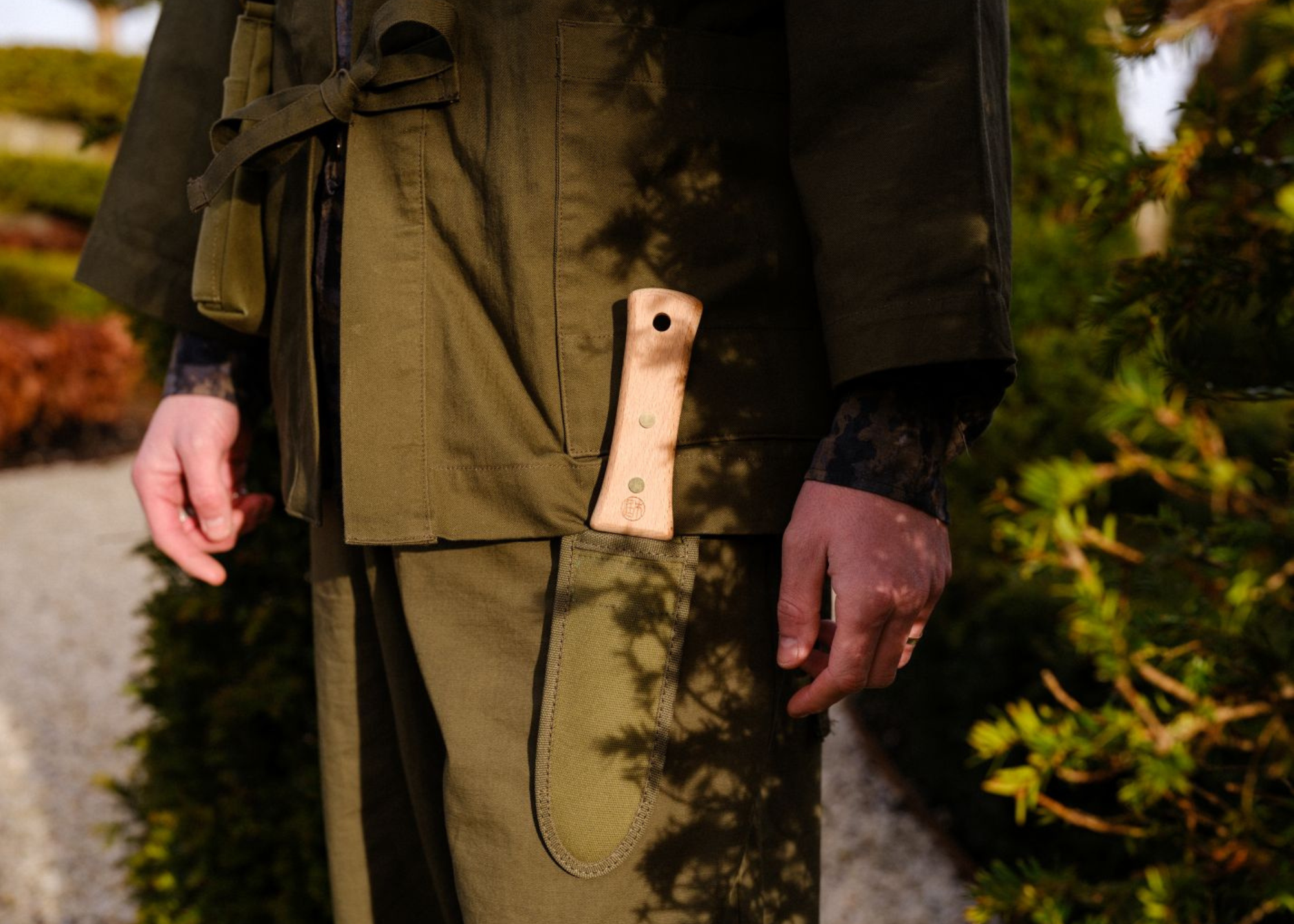 a man dressed in khaki with a hori hori knife in his pocket
