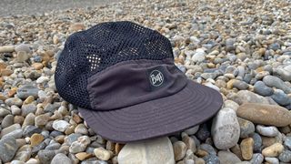 The Buff 5-Panel Air Cap on a pebbly beach.