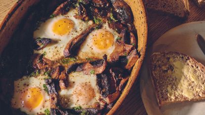 A dish of bake mushrooms with eggs next to a plate with buttered toast