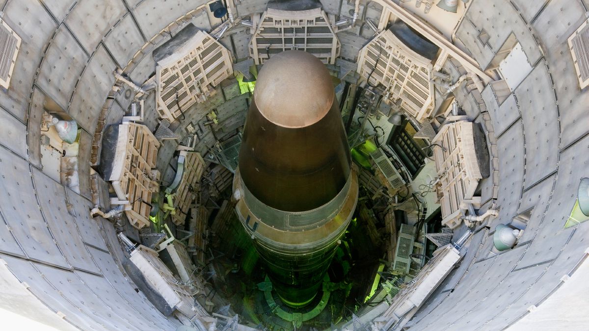A large metal missile is seen down in a tall cylindrical missile silo.