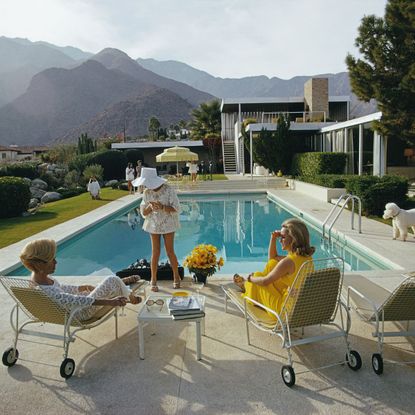 Former fashion model Helen Dzo Dzo Kaptur (in white lace), Nelda Linsk (in yellow), wife of art dealer Joseph Linsk, and actress Lita Baron (in white sunhat) at the Kaufmann Desert House in Palm Springs, California, January 1970. The Linsks are the current owners of the house. (Photo by Slim Aarons/Getty Images)