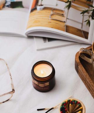 A small brown lit candle with matches next to it, glasses to the left, and an open magazine with a kitchen scene above it