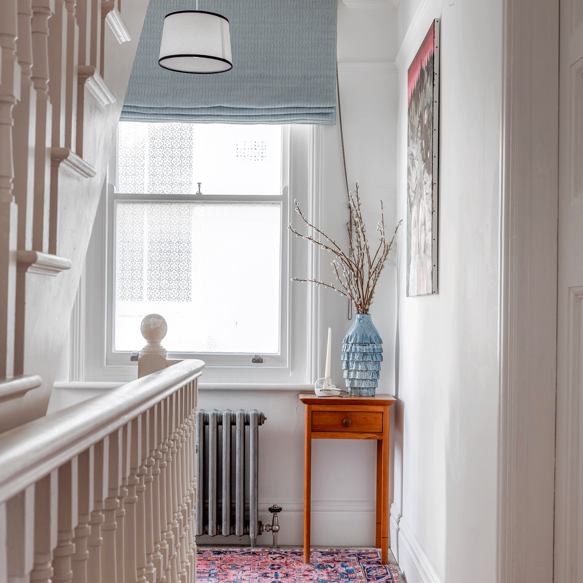 the landing in a home beside a stair well going up and down with a window covered in patterned window film and a patterned rug on the floor