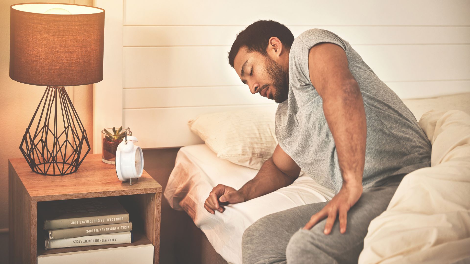 A man wearing grey pyjamas waking up with cramp at night due to dehydration