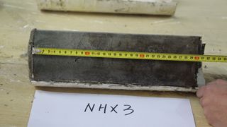 The sediment core used in the study laid down on a work surface with a tape measurer placed against it. The core is annotated NHX3.