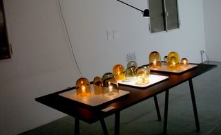 A table featuring twelve glass candle covers covering lightbulbs that are switched on.