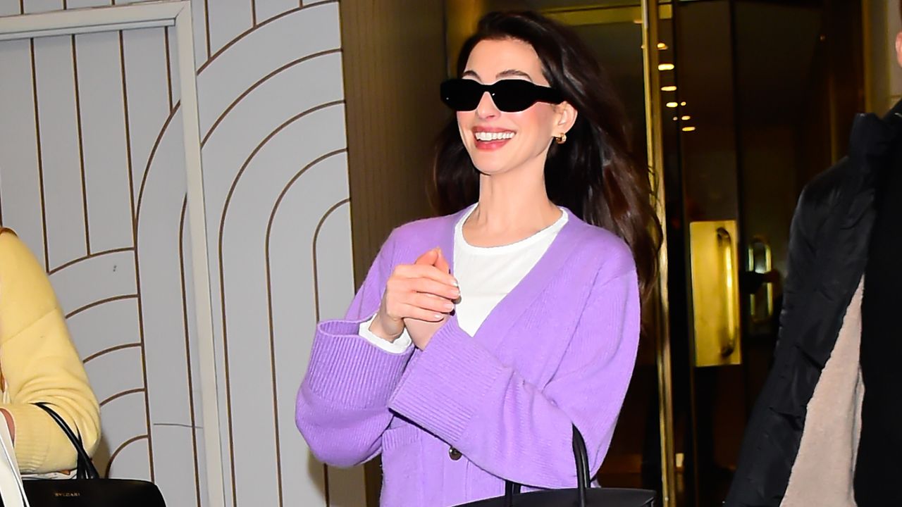 Anne Hathaway in chunky sneakers, purple cardigan, white pants, and a Birkin bag.