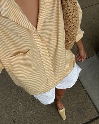 Woman wearing white linen shorts and yellow striped button down shirt.