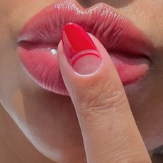 Close up of lips with a painted pink fingernail touching the lips