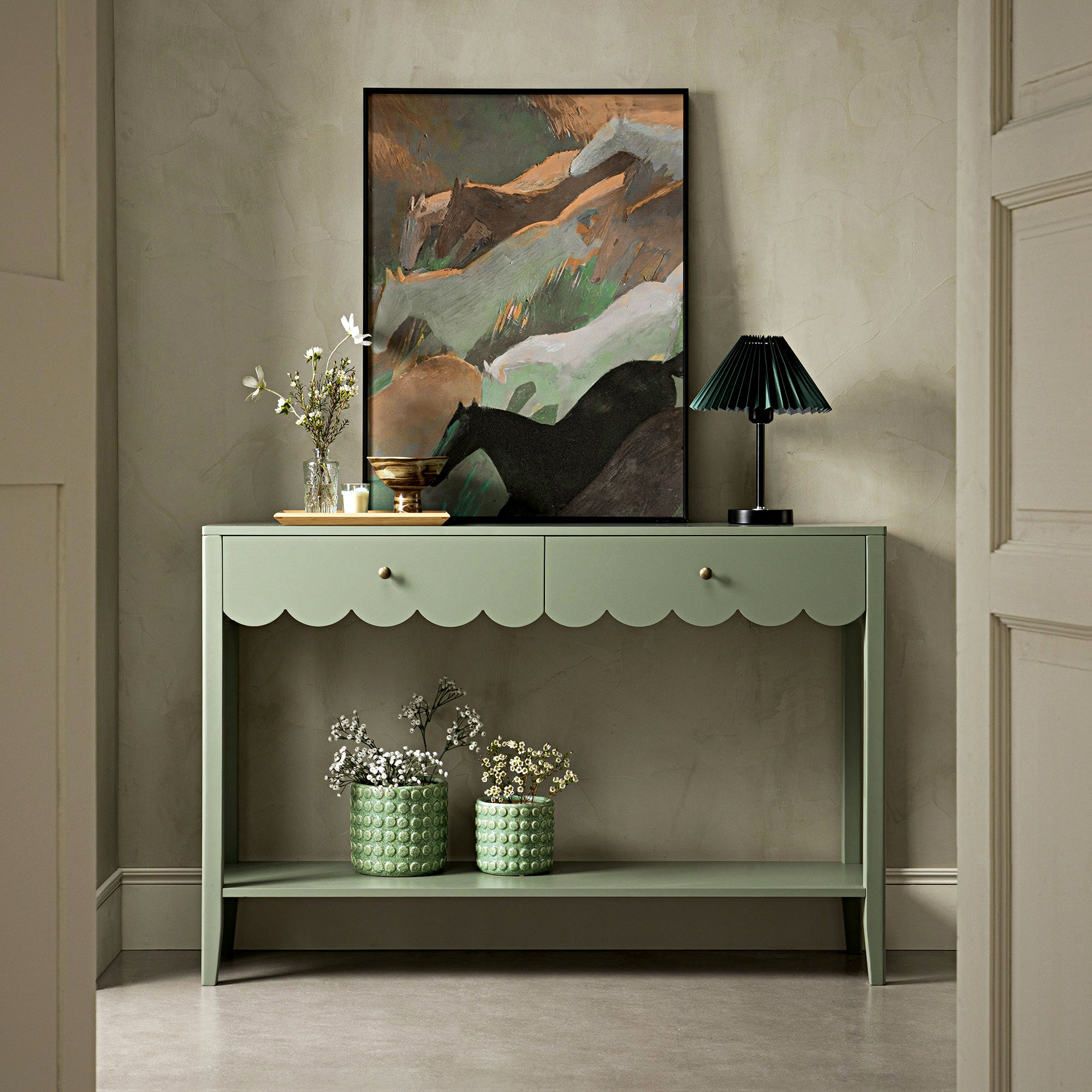 Green hallway table with abstract wall art and a black lamp