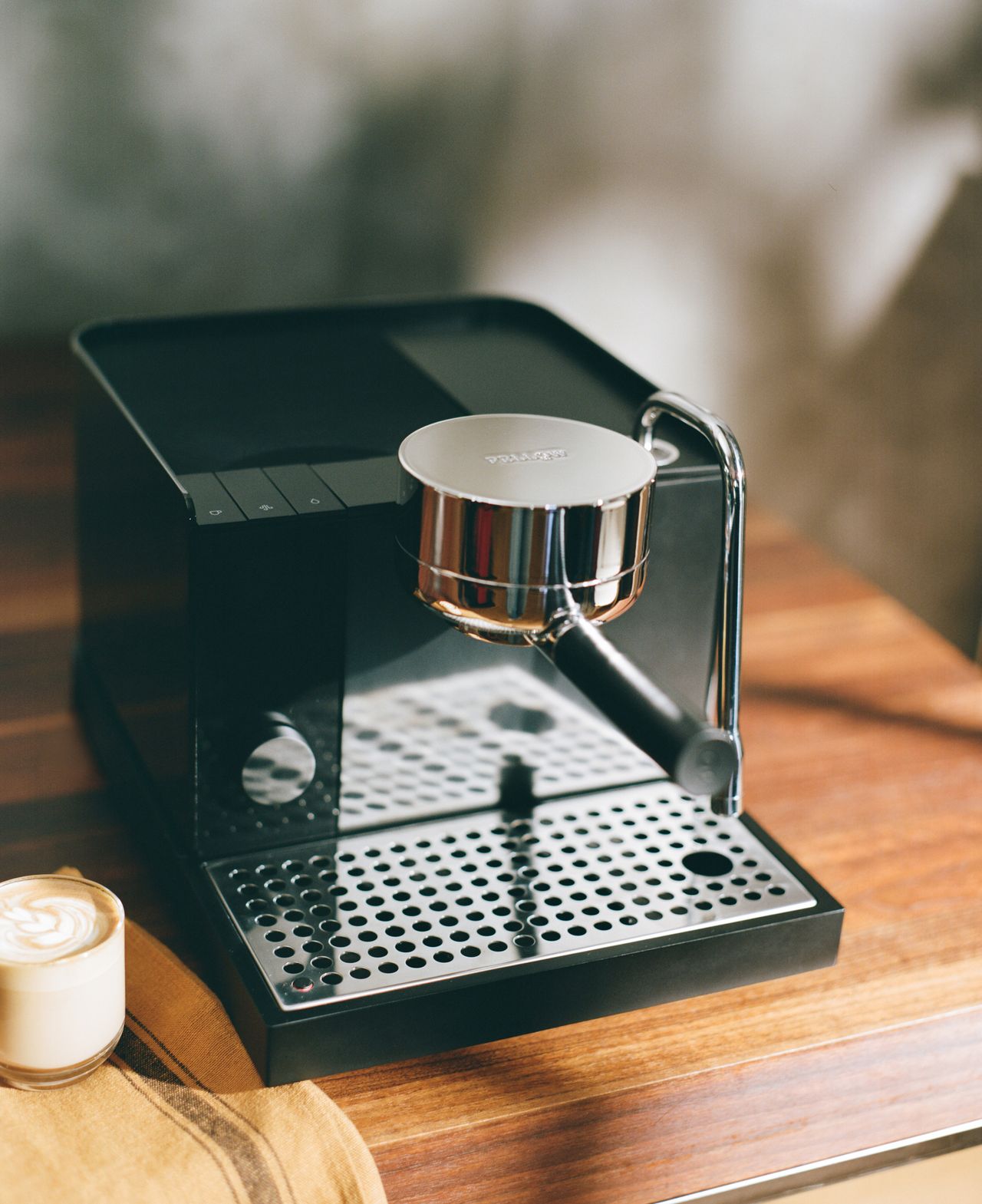 Image of the black Fellow Series 1 espresso machine on a wooden countertop with a latte next to it.
