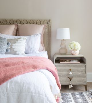 neutral bedroom with coral accents, textured headboard and side table, grey textured rug, stone walls