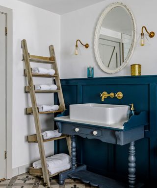 Wooden ladder shelf against wall in bathroom with white towels stored on each shelf