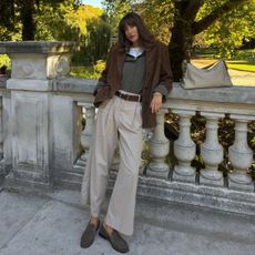 A woman wearing a brown suede blazer, plaid shirt, wide-leg chino trousers and loafers.