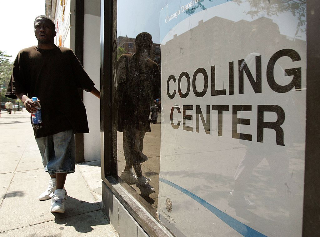 A man wearing a brown shirt and gray pants exits a building with a white sign saying
