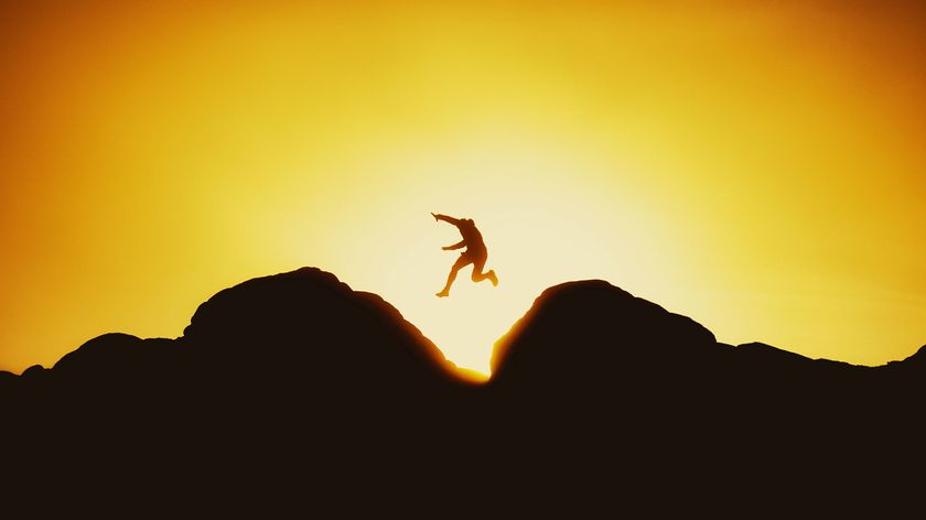 Silhouette of a person jumping between two rocks against a vibrant orange sunset sky, capturing a moment of freedom and adventure