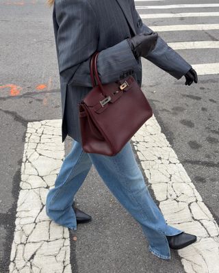 Woman wears blazer, jeans, black gloves and burgundy birkin bag