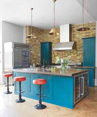 Bright blue kitchen units with red bar stools in an exposed brick and white kitchen space.