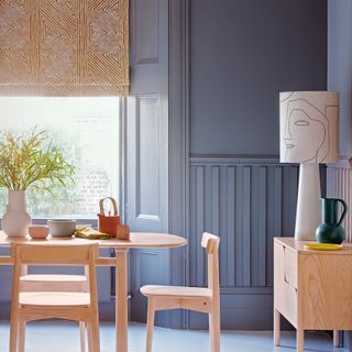 Grey dining room with pale wood furniture, oversized lamp on sideboard and patterned blind on window