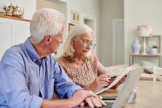A senior couple reviews paperwork while sitting at their dining room table.