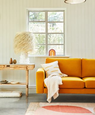 A living room with a turmeric yellow sofa in front of a white paneled wall