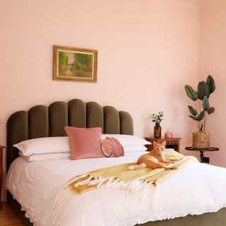 Double bed with green scalloped headboard in bedroom with pale pinks walls