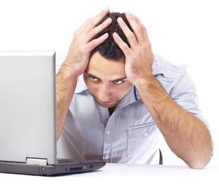 A man sitting at his computer has a headache.