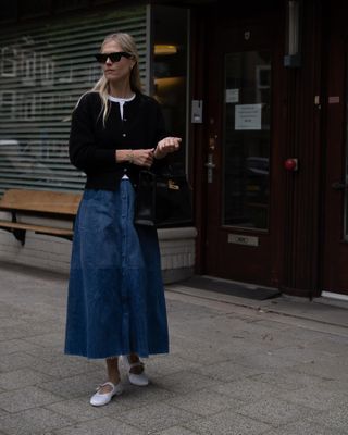 Woman wearing flat Mary Janes with a long denim skirt and a black cardigan.