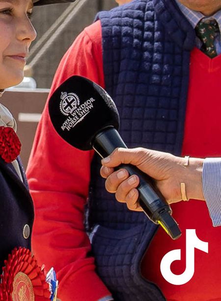 A rider has a large microphone branded to Royal Windsor Horse Show held in front of them by a third party who is off camera