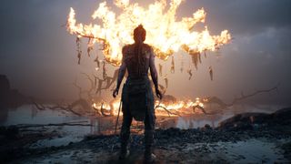 Hellblade's Senua stands in front of a burning tree with her back to us