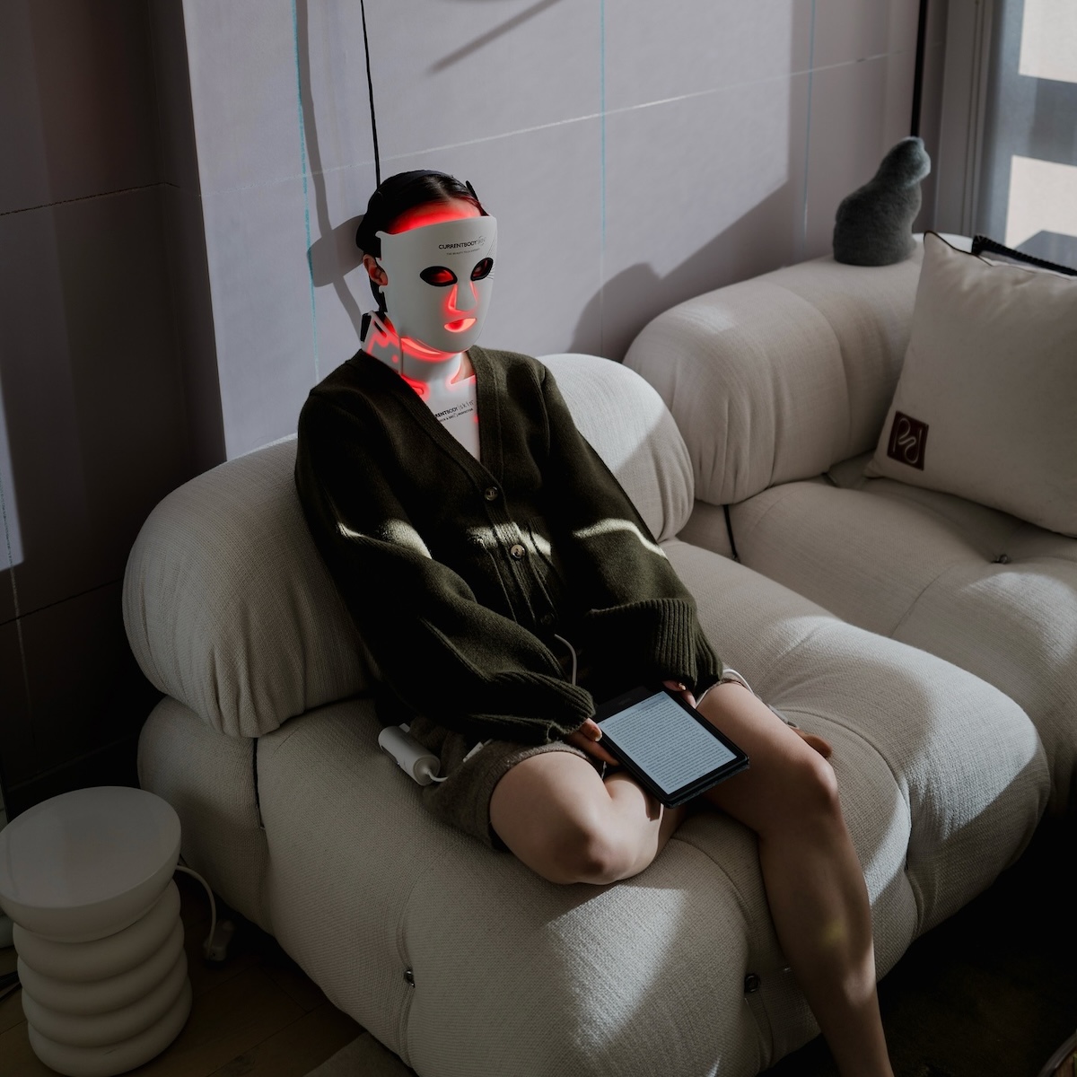 Woman sitting on a couch while wearing an LED face mask.