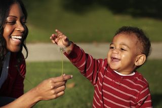 A little boy plays with a dandelion while Mom watches.