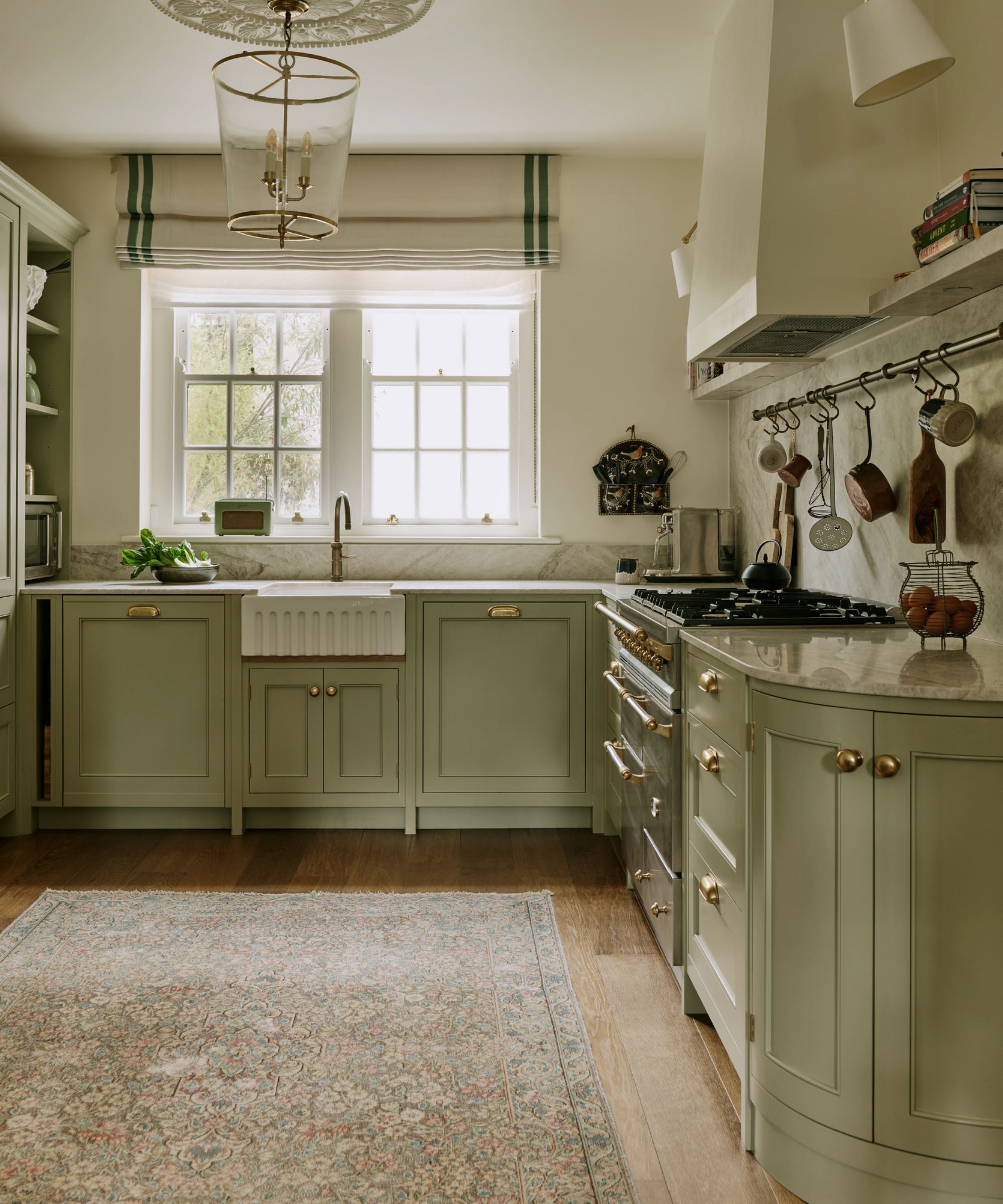 a traditional shaker kitchen in a london home painted in a soft green hue with a fluted sink, vintage rug, plaster cooker hood and rangecooker
