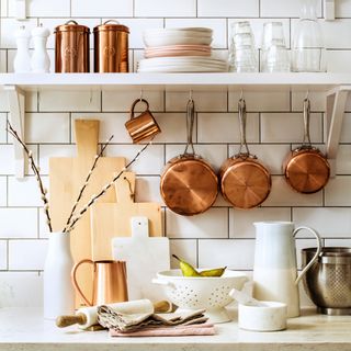 Open kitchen shelving against subway tile with copper pots and pans hanging up