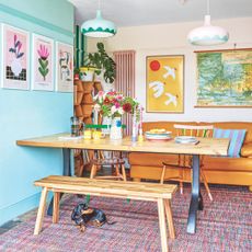 Dining room table and orange sofa on top of a colourful rug with a sausage dog sitting on it