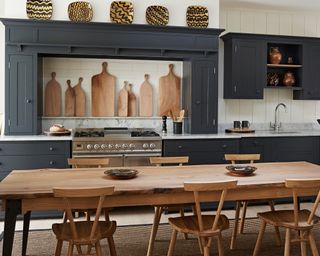 A Shaker style kitchen with a long wooden dining table and decorative plates above the fireplace
