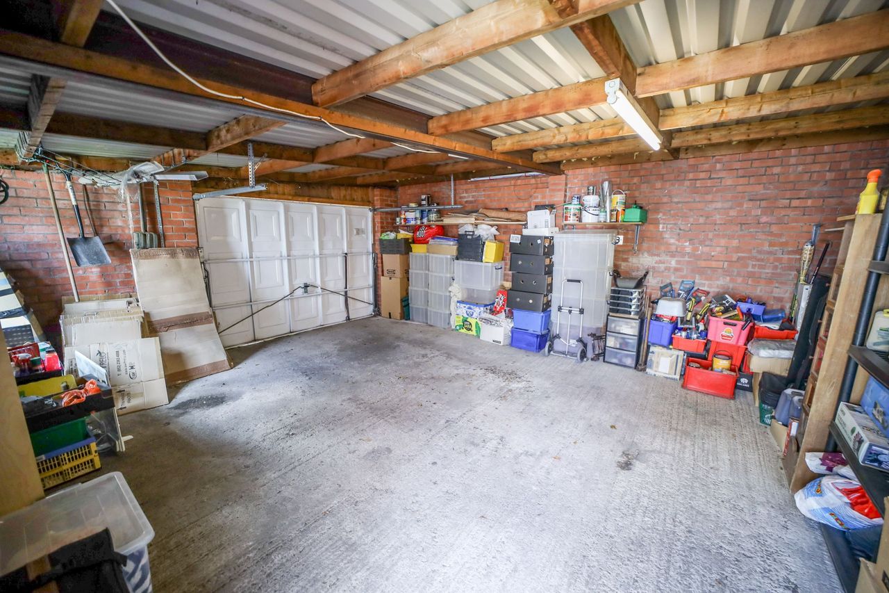 The garage shows a cement floor, wooden beams above and metal roofing as well as a white large garage door
