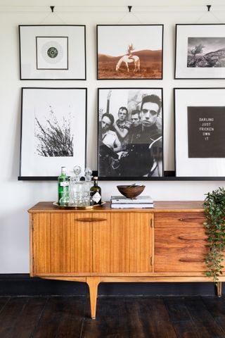 A wood sideboard with books, ornaments, and a drinks tray in a living room with wall art