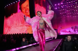 Topless man in feather coat and metallic pink trousers singing