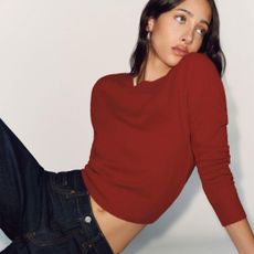 Reformation model wearing red sweater and dark jeans looking over her shoulder 