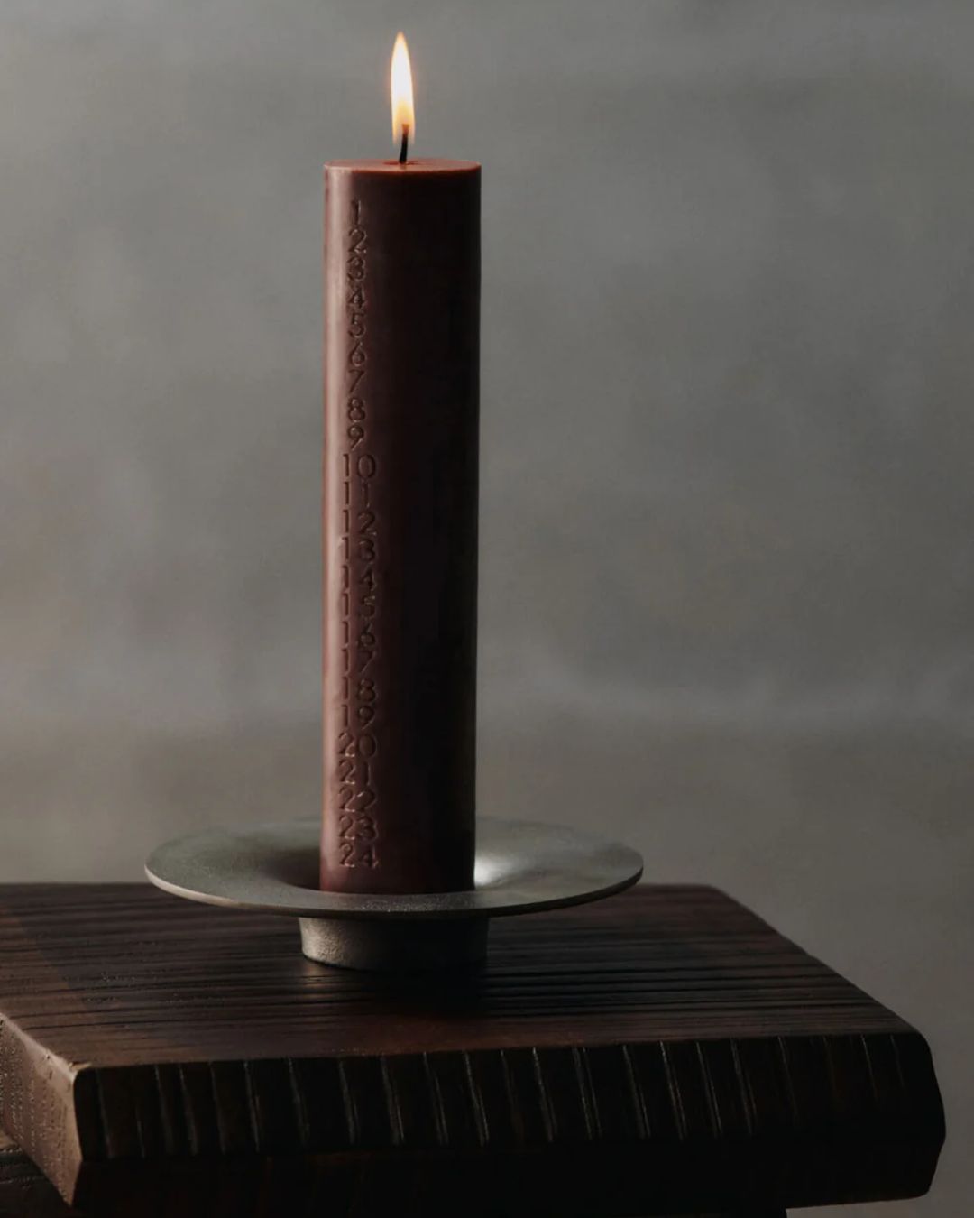 Soothe Block Candle Holder in Aluminium, holding a numbered, lit-up red candle.